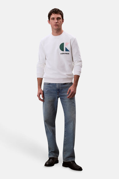 Sweat-shirt à col rond blanc de Calvin Klein, porté avec un jean décontracté bleu et des chaussures noires.