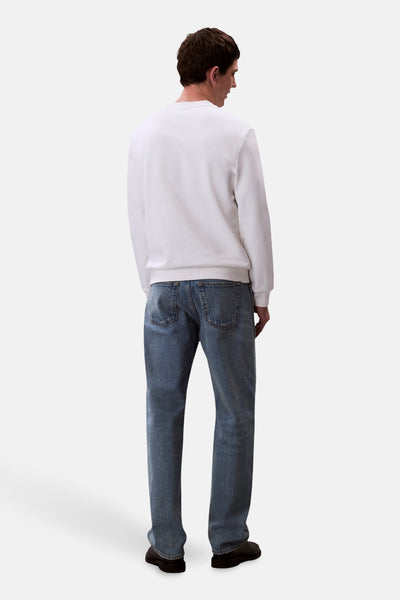 Sweat-shirt blanc de Calvin Klein, porté avec un jean bleu et des chaussures noires, vue de dos.
