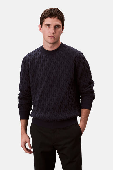 Sweat bleu marine de Calvin Klein, avec un motif texturé discret, porté avec un pantalon noir.
