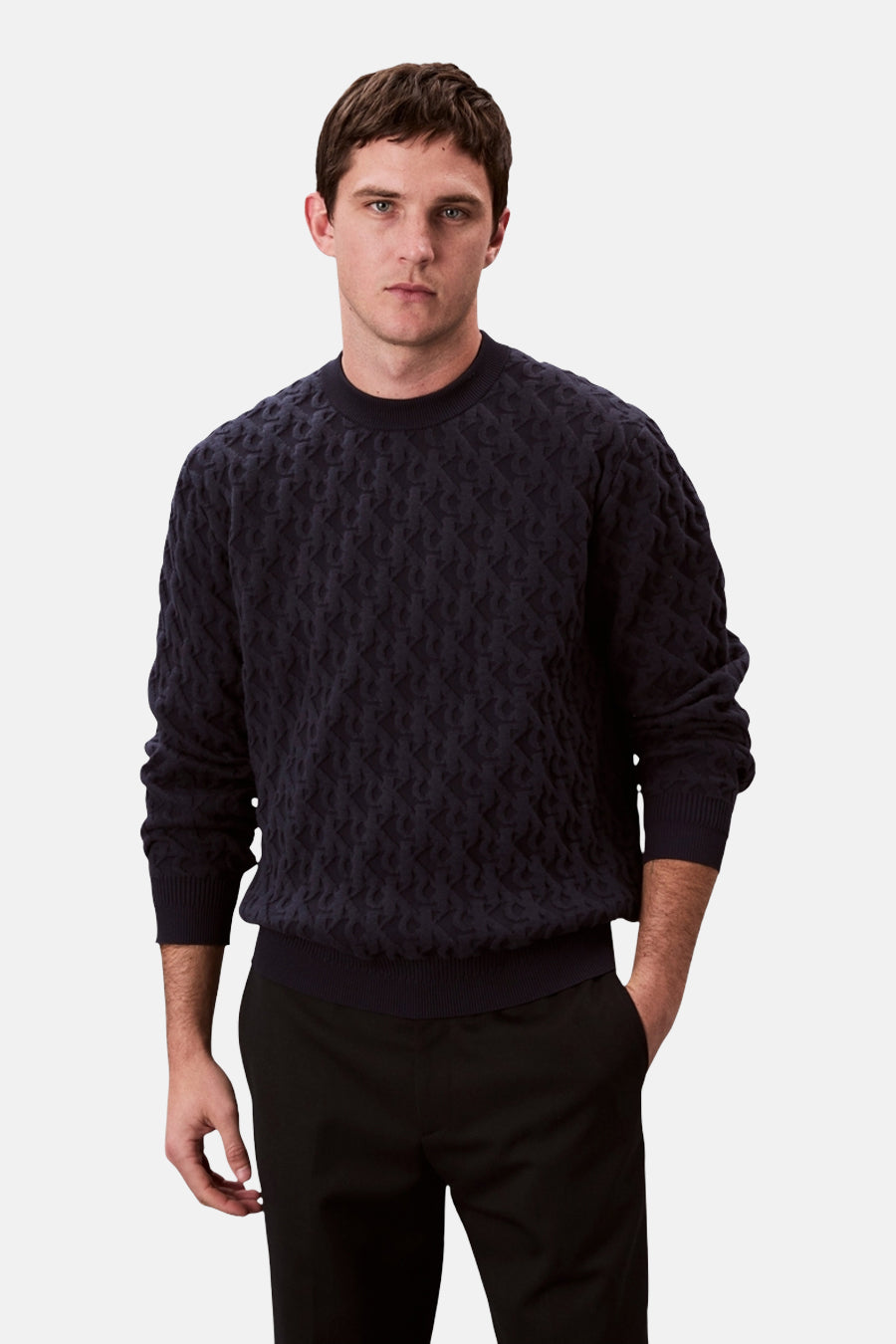 Sweat bleu marine de Calvin Klein, avec un motif texturé discret, porté avec un pantalon noir.
