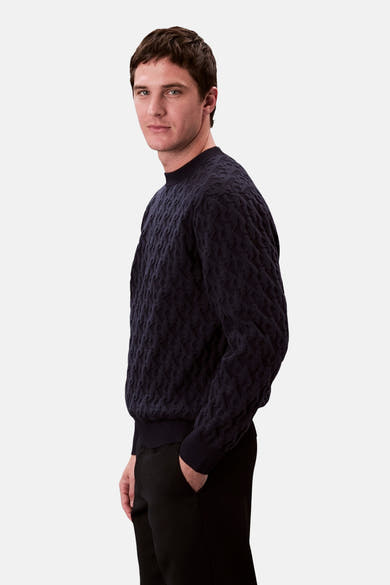 Sweat bleu de Calvin Klein, avec motif texturé, porté avec un pantalon noir, en vue latérale.