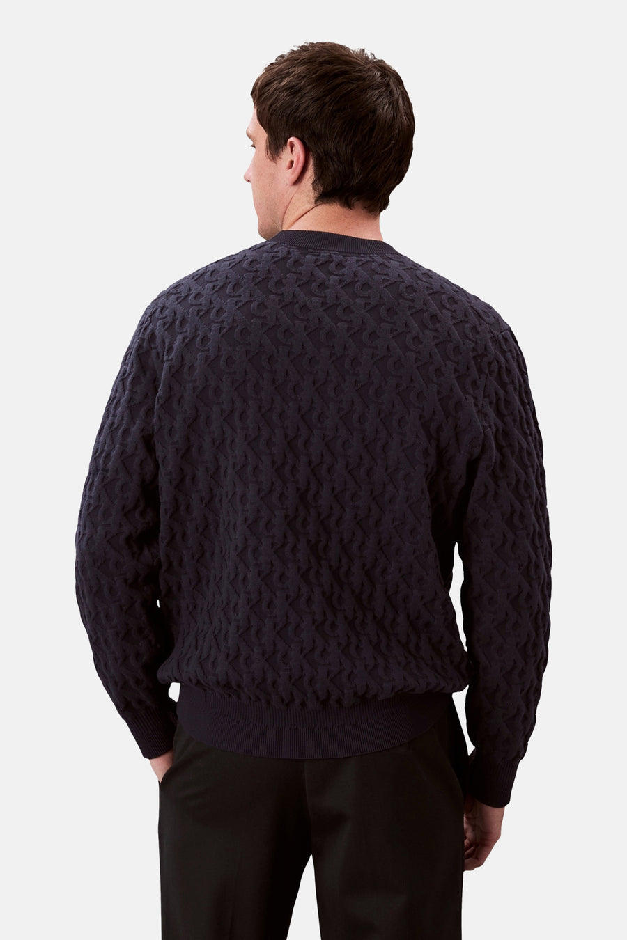 Sweat bleu col rond de Calvin Klein avec un motif texturé, porté avec un pantalon noir, vue de dos.