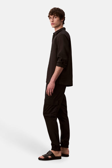 Pantalon cargo noir par Calvin Klein, porté avec une chemise noire et des sandales en cuir, vue de côté.