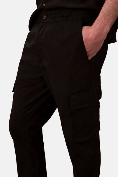 Pantalon cargo noir par Calvin Klein, avec une poche cargo sur la jambe, porté avec une chemise noire.