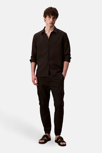 Pantalon cargo noir de Calvin Klein, avec poches latérales et coupe ajustée, porté avec une chemise boutonnée noire.