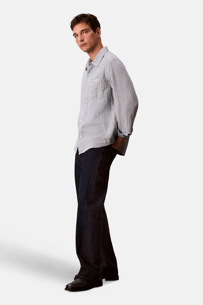Chemise à manches longues bleue en coton by Calvin Klein, avec motif rayé et manches retroussées, portée avec un jean foncé.