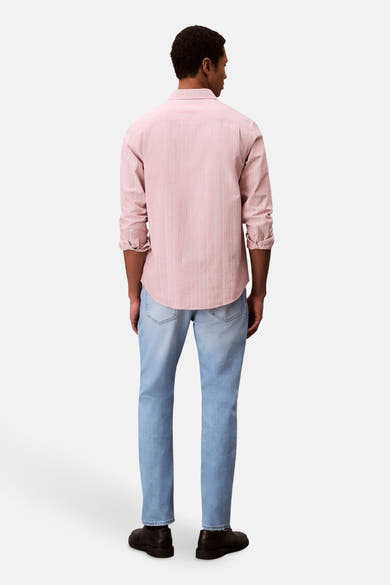 Slim jeans van lichtblauw denim van Calvin Klein, gedragen met een roze gestreept overhemd en zwarte schoenen.