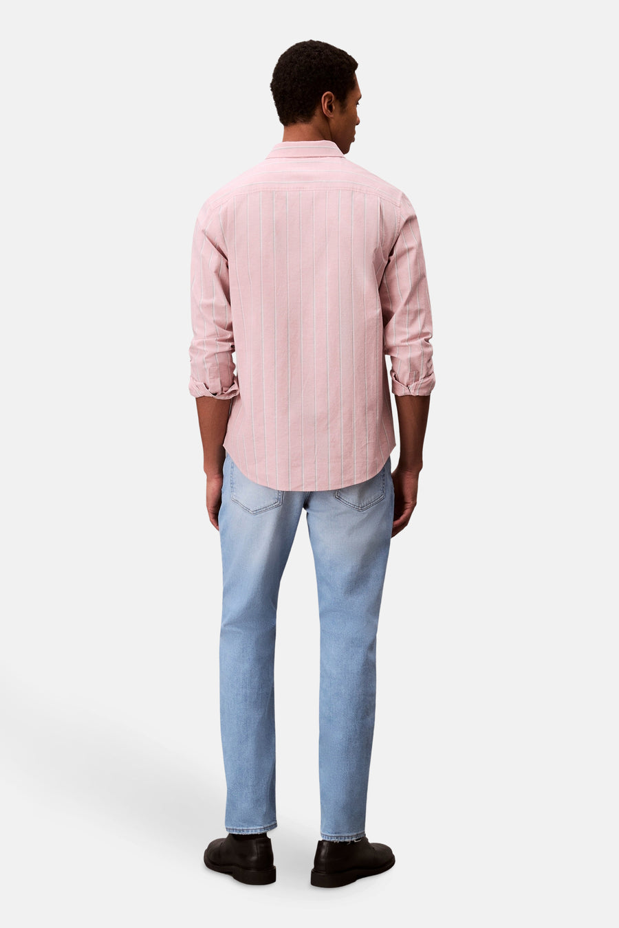 Slim jeans van lichtblauw denim van Calvin Klein, gedragen met een roze gestreept overhemd en zwarte schoenen.