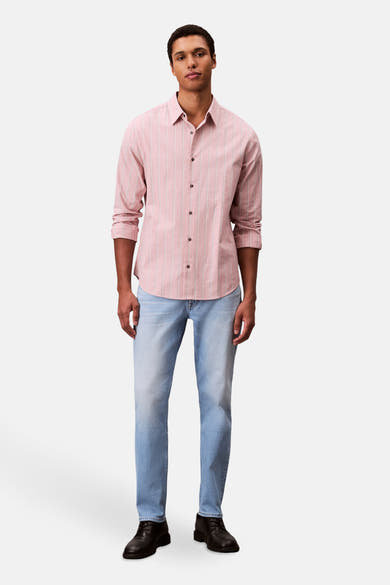 Slim jeans van lichtblauw denim van Calvin Klein, gedragen met een roze gestreept overhemd en zwarte schoenen.