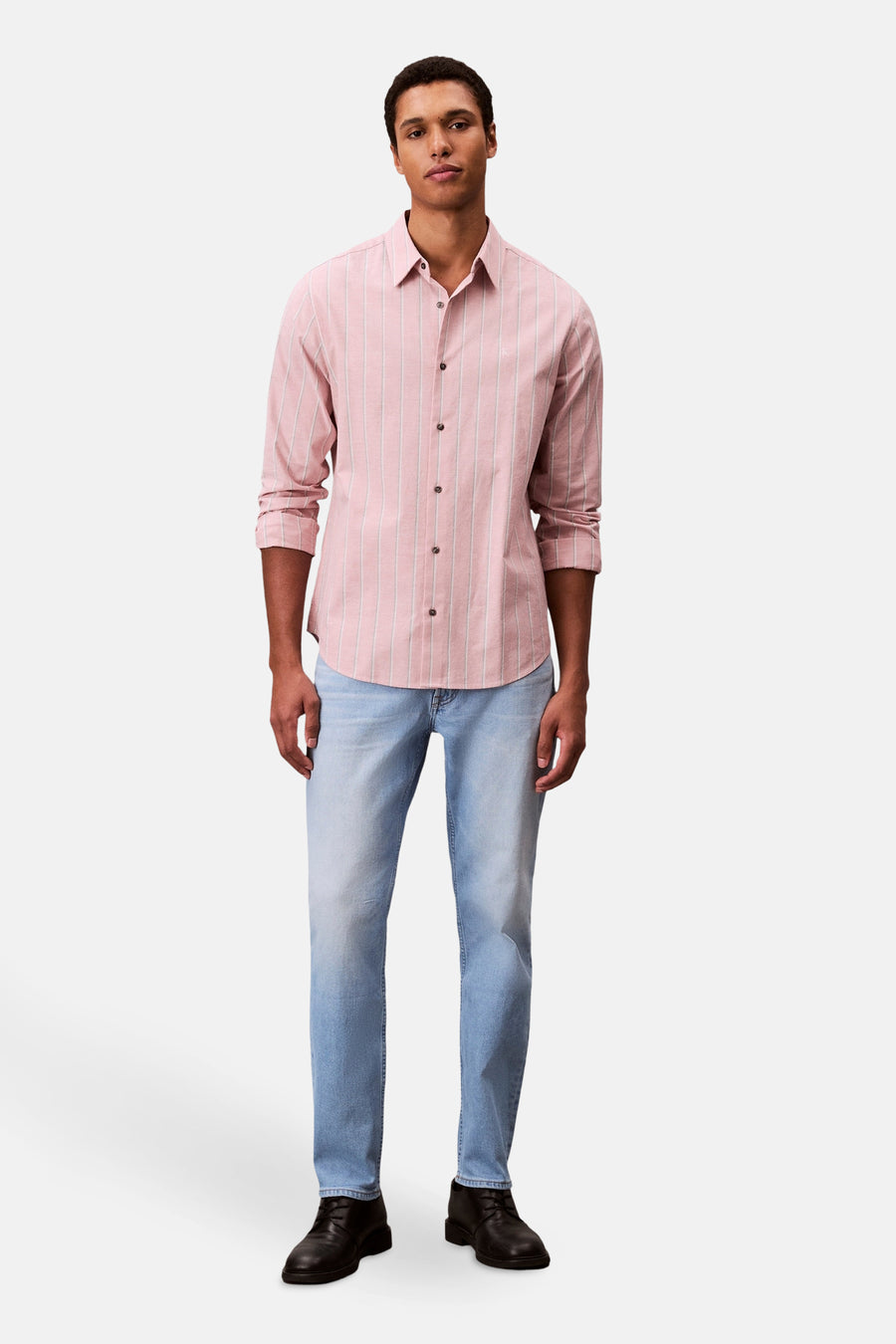 Slim jeans van lichtblauw denim van Calvin Klein, gedragen met een roze gestreept overhemd en zwarte schoenen.