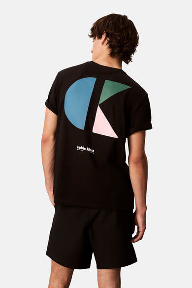 T-shirt à manches courtes noir de Calvin Klein avec motif graphique au dos, porté avec un short noir.
