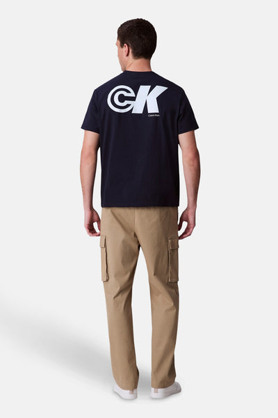 Blauw T-shirt met korte mouwen van Calvin Klein met een logo op de rug, gedragen met een beige cargobroek.