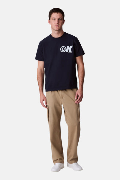 Marineblauwe T-shirt met korte mouwen van Calvin Klein, met een logo op de borst, gedragen met een beige cargobroek.