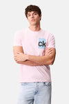 T-shirt rose à manches courtes de Calvin Klein, porté avec un jean bleu clair, modèle posant les bras croisés.
