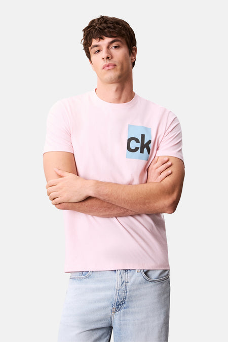 Roze T-shirt met korte mouwen van Calvin Klein, gedragen met een lichtblauwe jeans, model poseert met gekruiste armen.