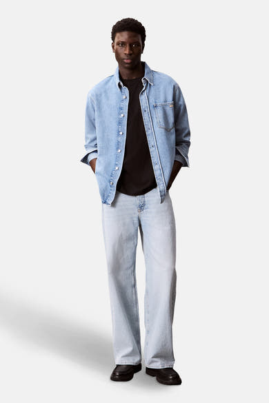 T-shirt noir à manches courtes de Calvin Klein, porté avec une chemise en jean ouverte et un pantalon ample en denim clair.