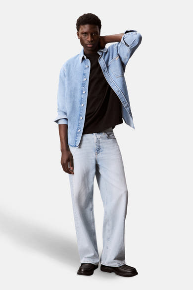 T-shirt noir à manches courtes de Calvin Klein, porté avec une chemise en jean clair et un pantalon en denim délavé.