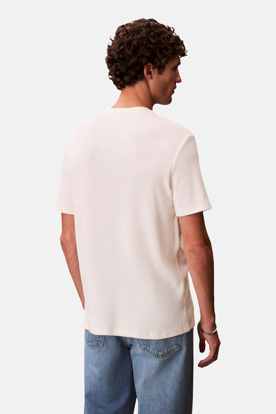 T-shirt jaune à manches courtes de Calvin Klein, avec une texture gaufrée, porté avec un jean bleu.
