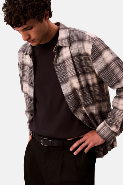 Chemise à manches longues grise à carreaux par Calvin Klein, portée ouverte sur un t-shirt noir, avec un pantalon noir.
