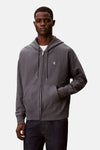 Blauwe Calvin Klein bodywarmer, met ritssluiting en capuchon, gedragen over een wit T-shirt en een donkere jeans.