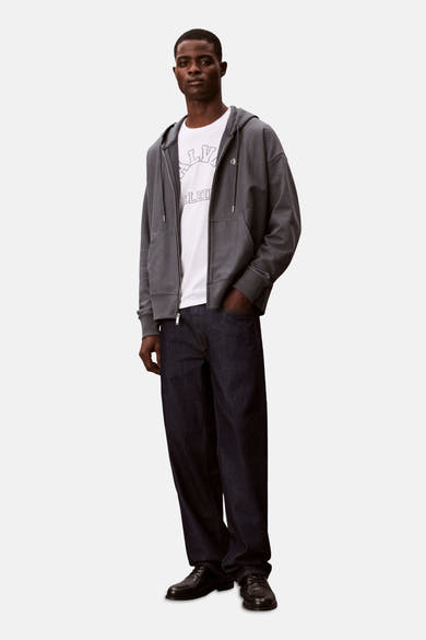 Blauwe Calvin Klein bodywarmer, gedragen over een wit T-shirt met print en een wijde donkerblauwe jeans.