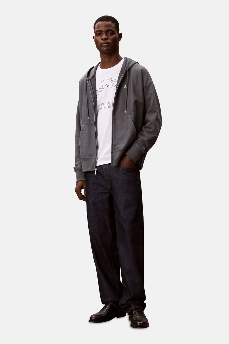 Blauwe Calvin Klein bodywarmer, gedragen over een wit T-shirt met print en een wijde donkerblauwe jeans.