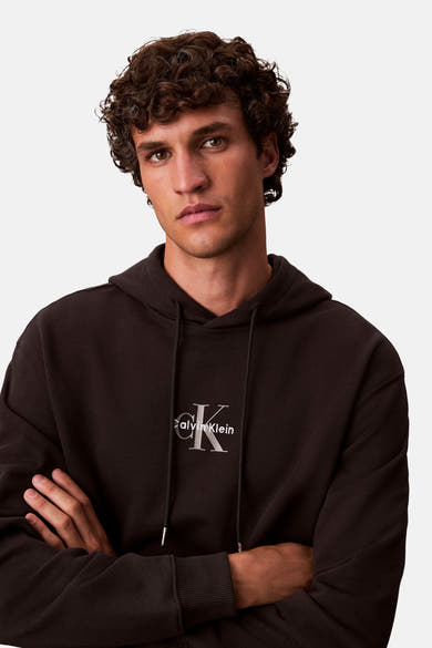 Zwarte Calvin Klein hoodie, gedragen door een man met gekruiste armen.