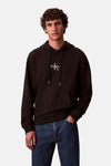 Zwarte Calvin Klein hoodie, gedragen met een blauwe spijkerbroek, op een effen achtergrond.