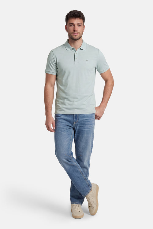 Polo bleu clair à manches courtes de Calvin Klein, porté avec un jean bleu et des chaussures décontractées beiges.
