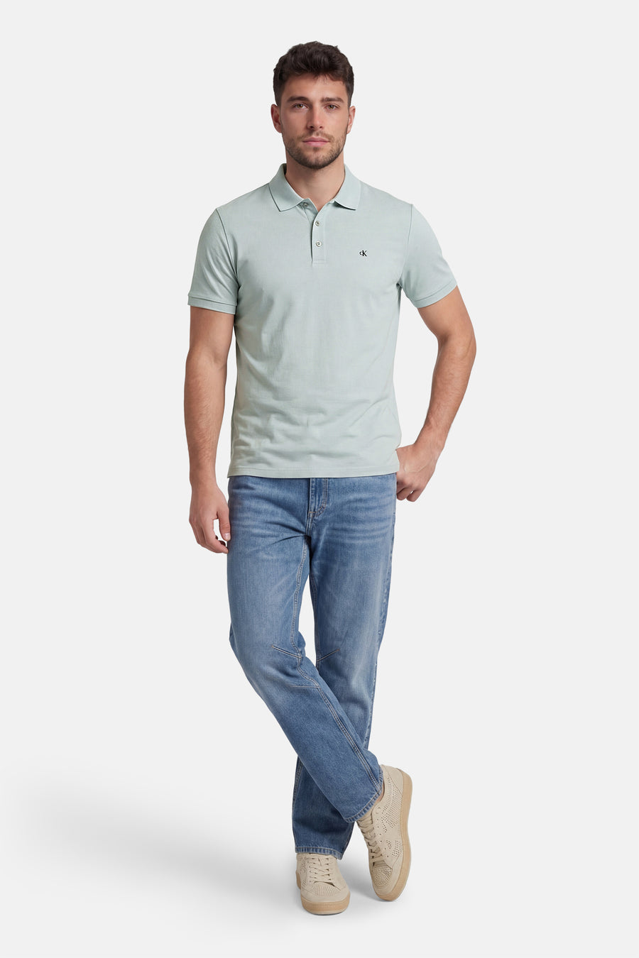Polo bleu clair à manches courtes de Calvin Klein, porté avec un jean bleu et des chaussures décontractées beiges.

