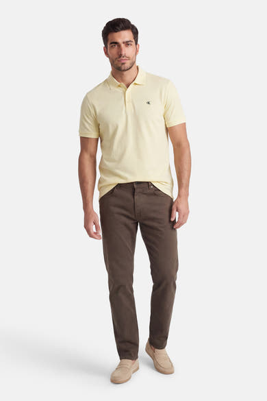 Gele poloshirt met korte mouwen van Calvin Klein, gedragen met een bruine broek en zandkleurige loafers.