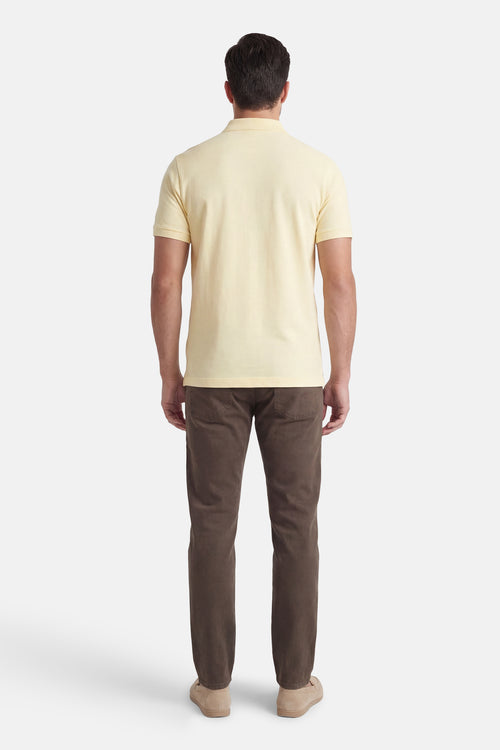 Polo à manches courtes jaune de Calvin Klein, porté avec un pantalon marron et des mocassins en daim, vue de dos.