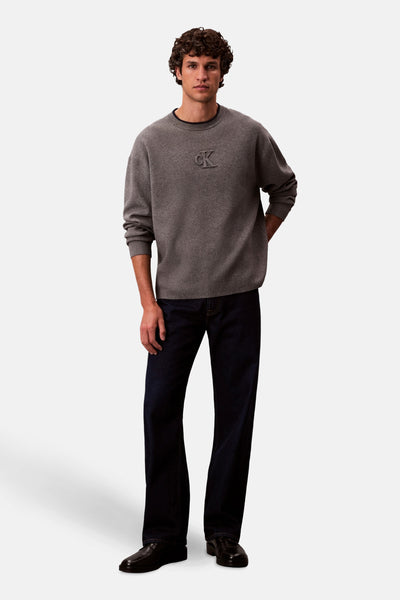 Grijze rondehals trui van Calvin Klein, gedragen met een donkere jeans en zwarte schoenen.