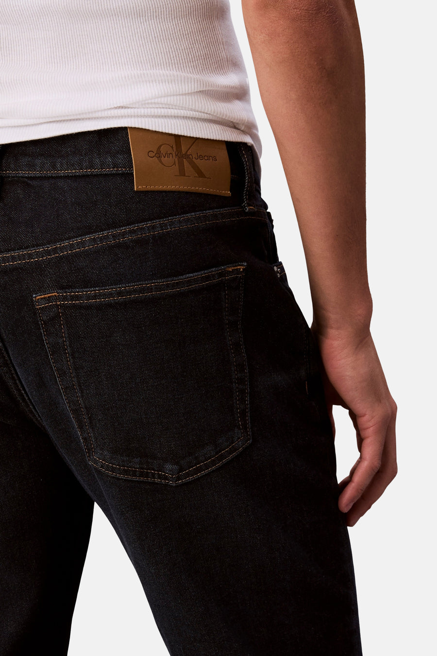 Jean fuselé bleu foncé de Calvin Klein, avec une étiquette en cuir apparente et une poche arrière sur un fond blanc.
