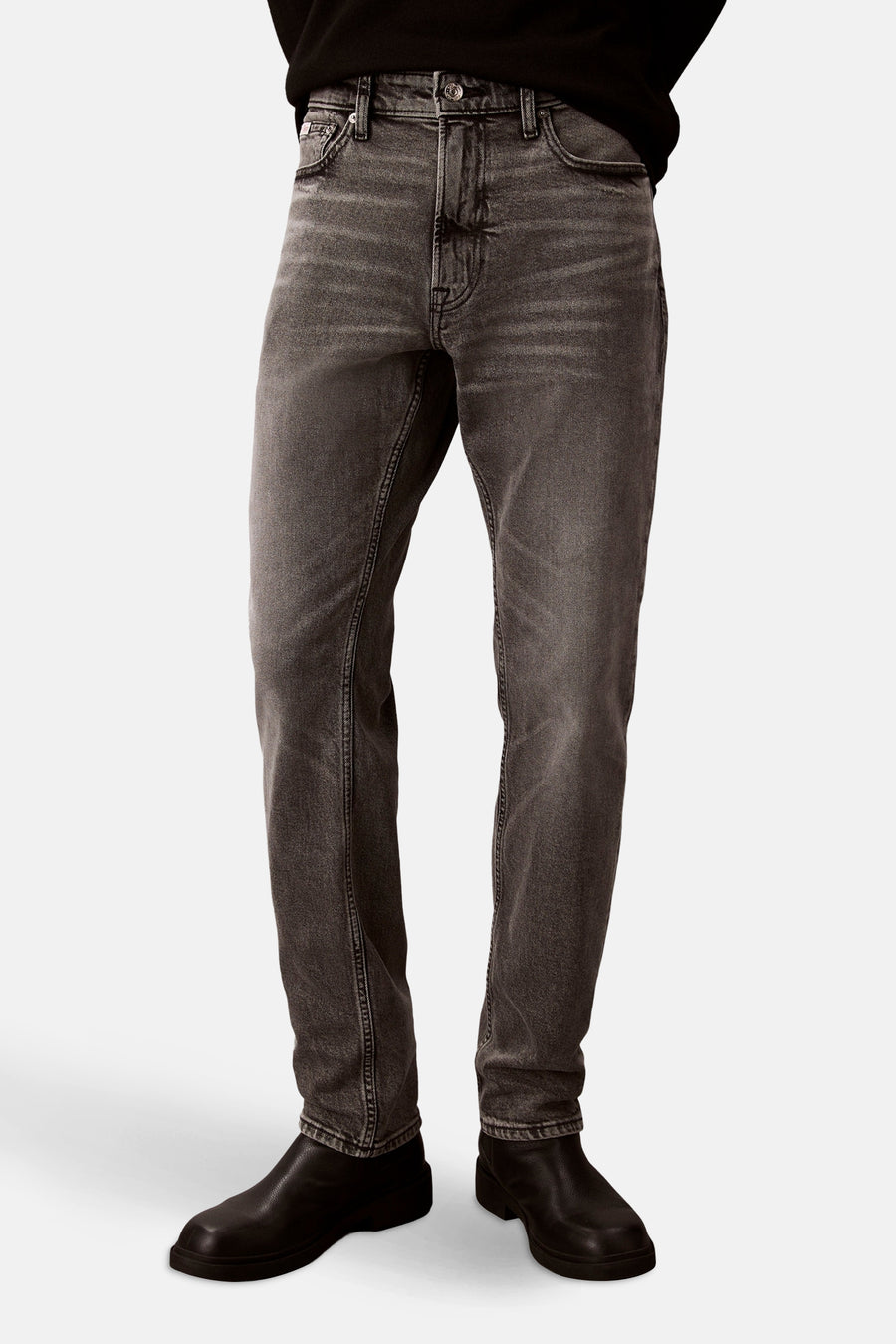 Slim jeans in middengrijs denim van Calvin Klein, gedragen met een zwarte trui en zwarte leren schoenen, in zijaanzicht.