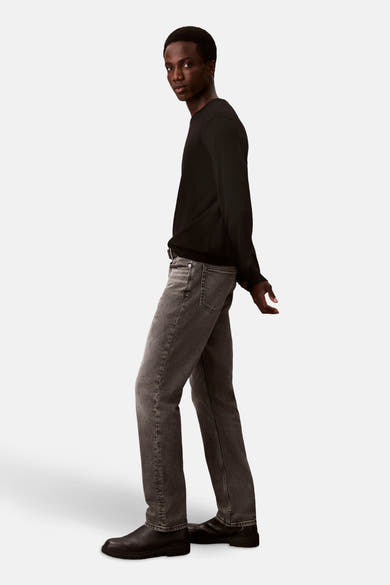 Jean slim en denim gris moyen de Calvin Klein, porté avec un pull noir et des chaussures en cuir noir, en vue latérale.
