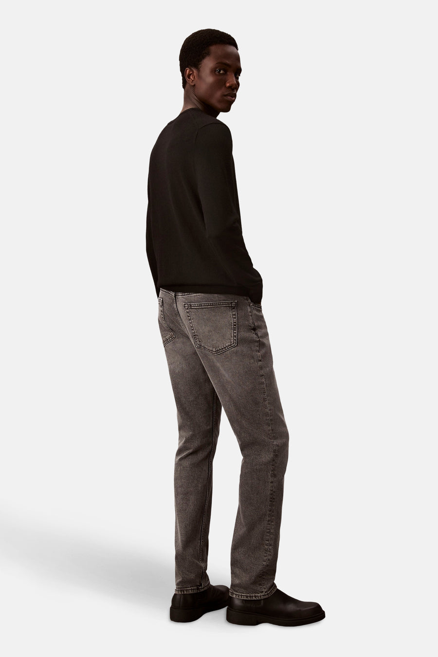 Middelgrijze slim fit jeans van Calvin Klein, gedragen met een effen zwart trui en zwarte schoenen.