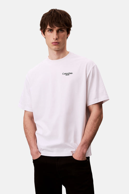 T-shirt blanc à manches courtes de Calvin Klein, porté avec un pantalon noir.
