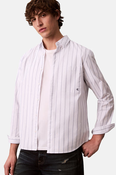 Chemise blanche à manches longues de Calvin Klein, rayée, portée avec un t-shirt blanc et un jean foncé.