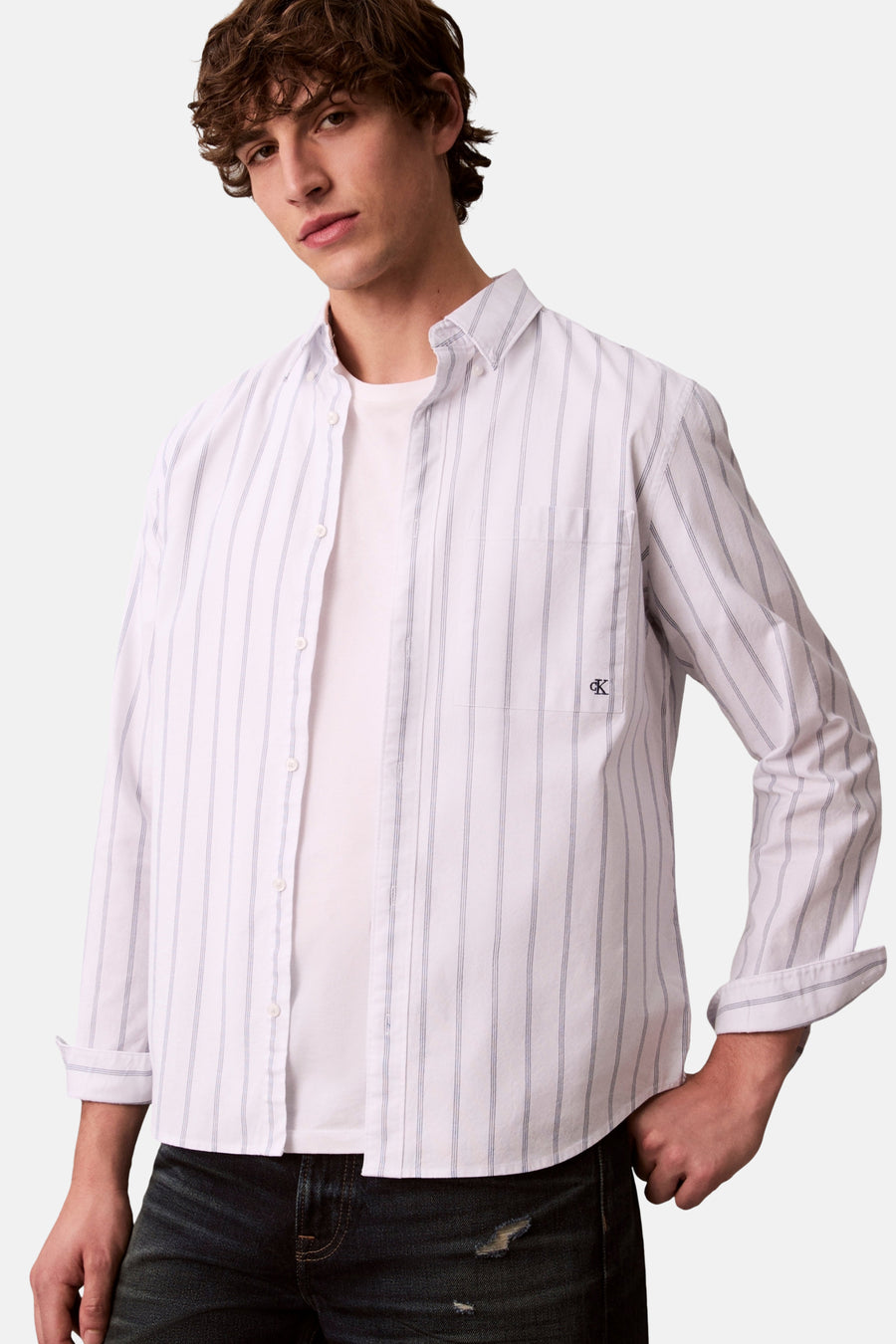 Chemise blanche à manches longues de Calvin Klein, rayée, portée avec un t-shirt blanc et un jean foncé.