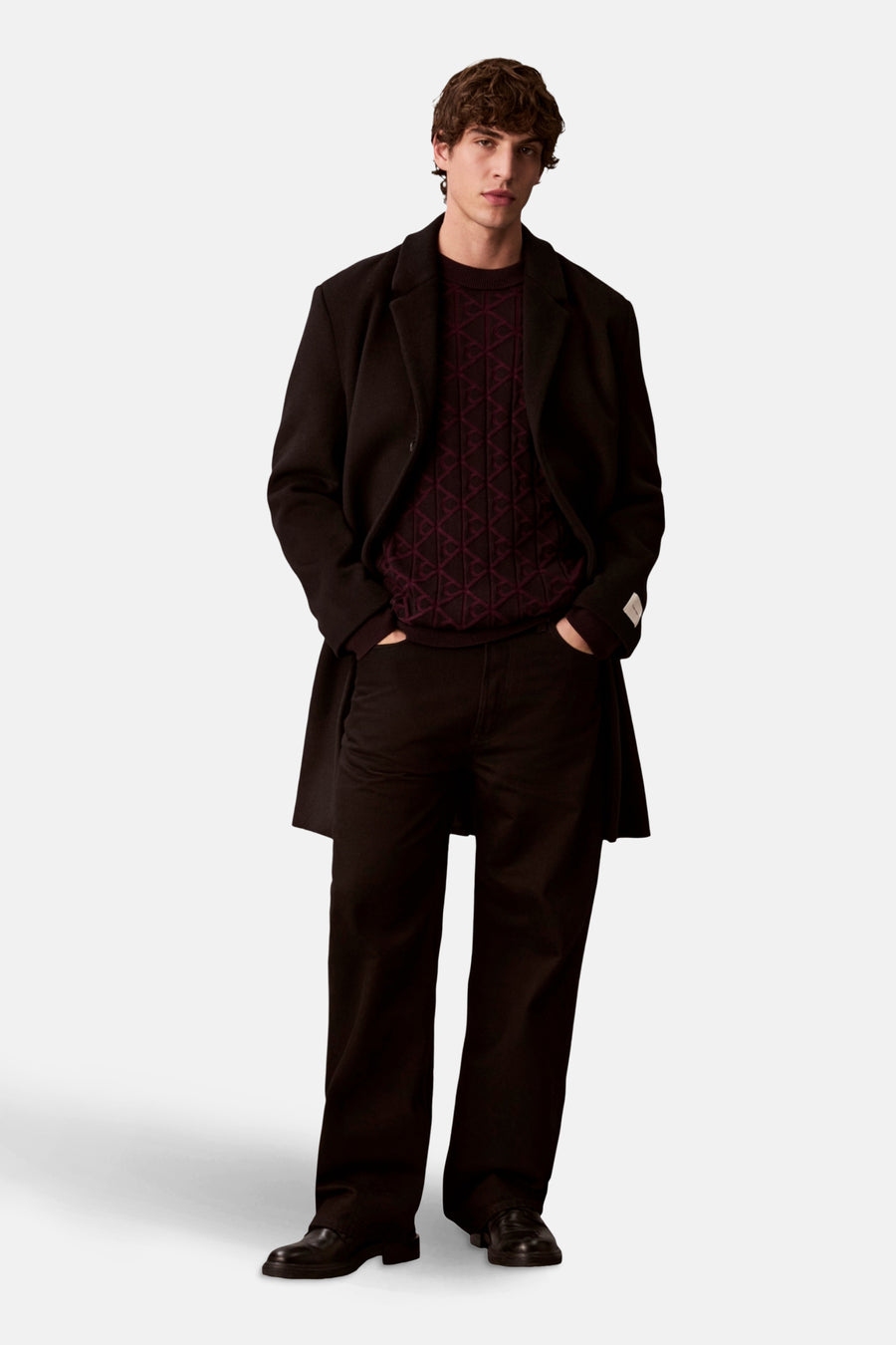 Sweat-shirt noir à col rond de Calvin Klein porté avec un manteau long et un pantalon noir.