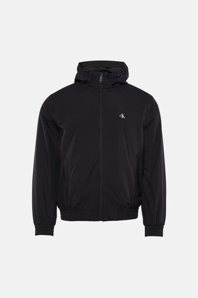 Zwarte regenjas van Calvin Klein, gedragen met een zwart T-shirt en een lichtgrijze spijkerbroek.