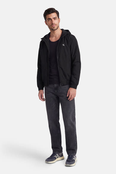 Veste de pluie noire de Calvin Klein, portée avec un t-shirt noir et un jean gris délavé.