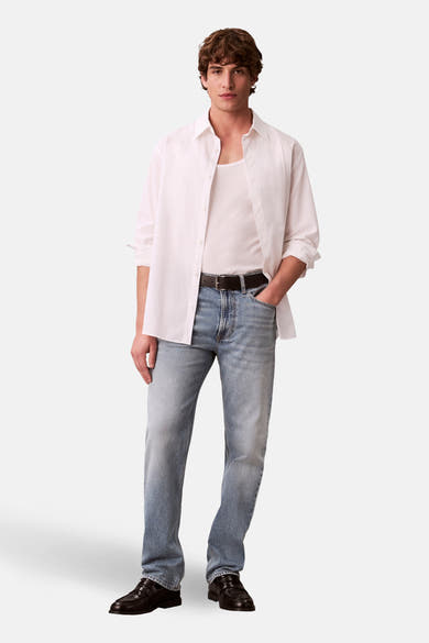 Rechte lichtblauwe spijkerbroek van Calvin Klein, gedragen met een wit overhemd en een tanktop.