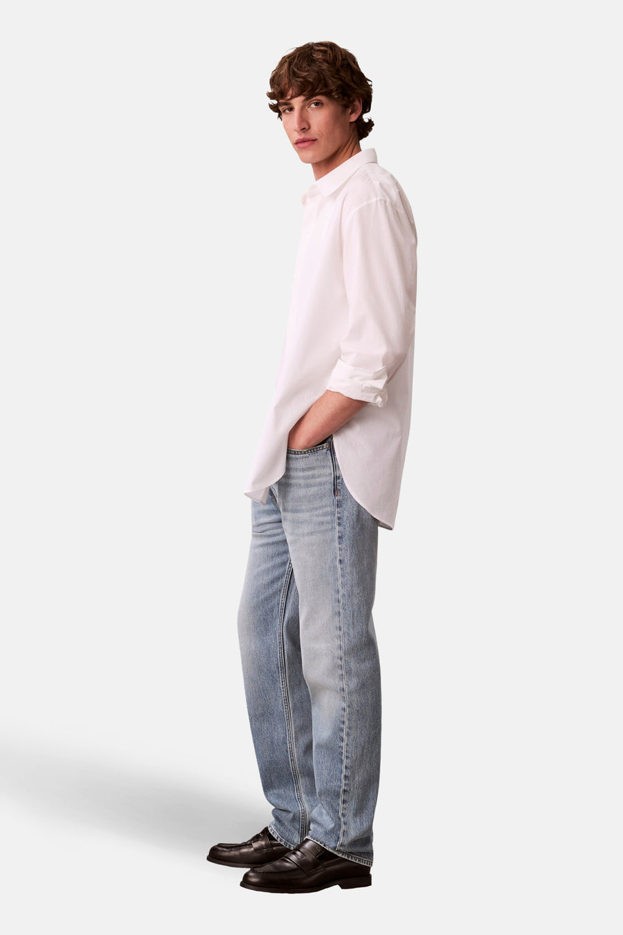 Rechte lichtblauwe spijkerbroek van Calvin Klein, gedragen met een wit overhemd en zwarte loafers, zij-aanzicht.