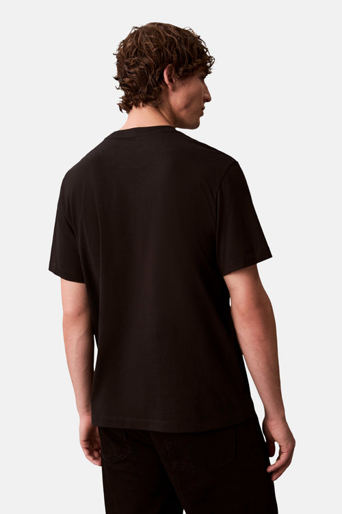 T-shirt noir à manches courtes de Calvin Klein, vu de dos, porté avec un pantalon noir.
