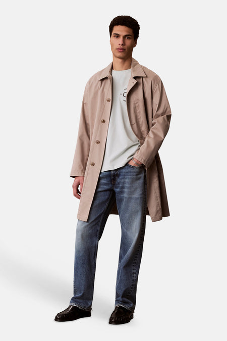 T-shirt bleu à manches courtes de Calvin Klein, porté avec un trench beige, un jean et des mocassins noirs.