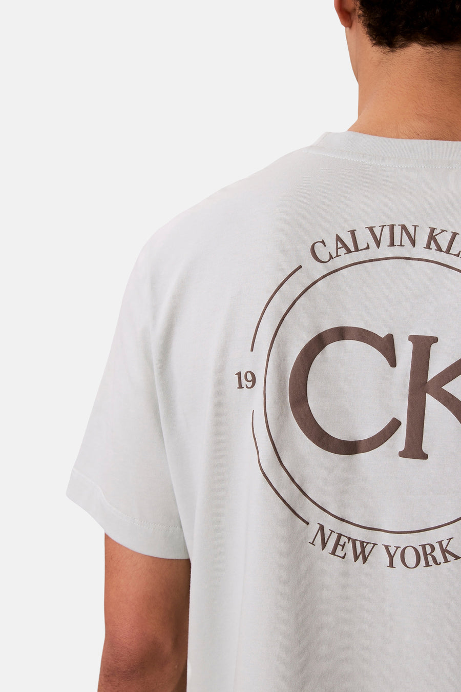 T-shirt bleu à manches courtes de Calvin Klein, avec un logo marron au dos.