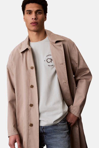Blauw T-shirt met korte mouwen van Calvin Klein met opdruk, gedragen onder een beige jas.