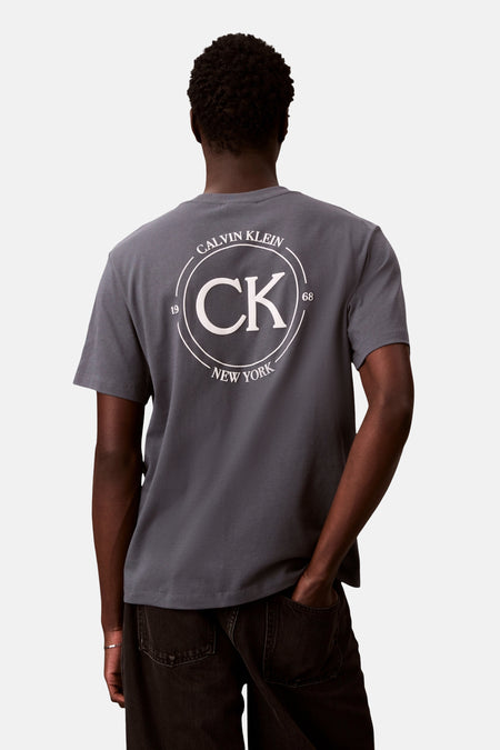 T-shirt gris à manches courtes de Calvin Klein, avec un logo circulaire imprimé au dos.